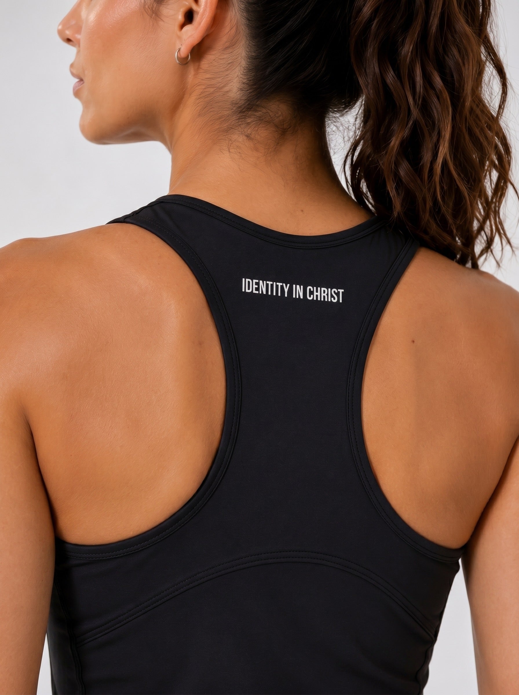 Image of Person wearing a black tank top with 'Identity in Christ' text on the back against a white background