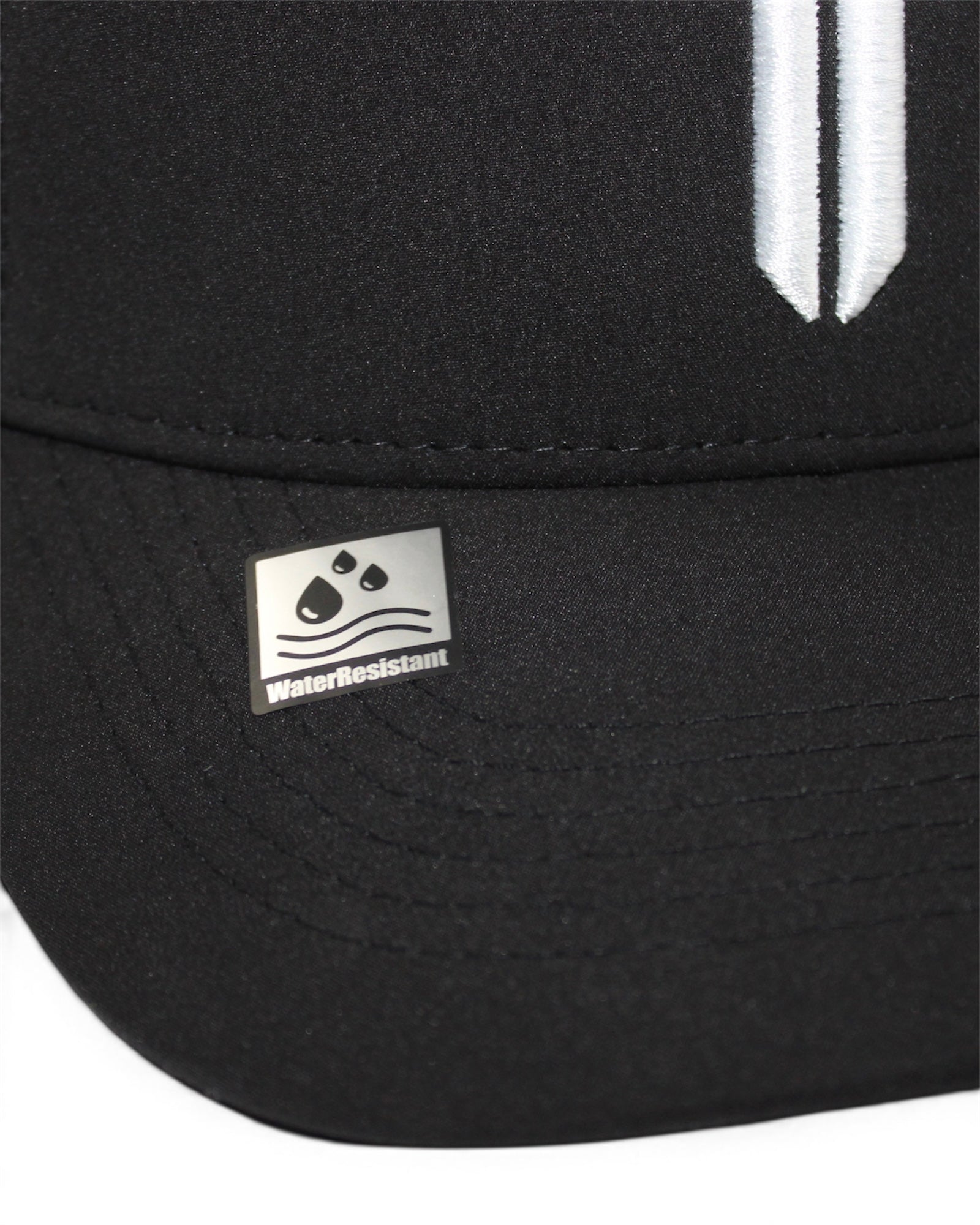 Image of Close-up of a black baseball cap showing a silver metal 'WaterResistant' badge on the brim and a white embroidered vertical stripe on the crown.