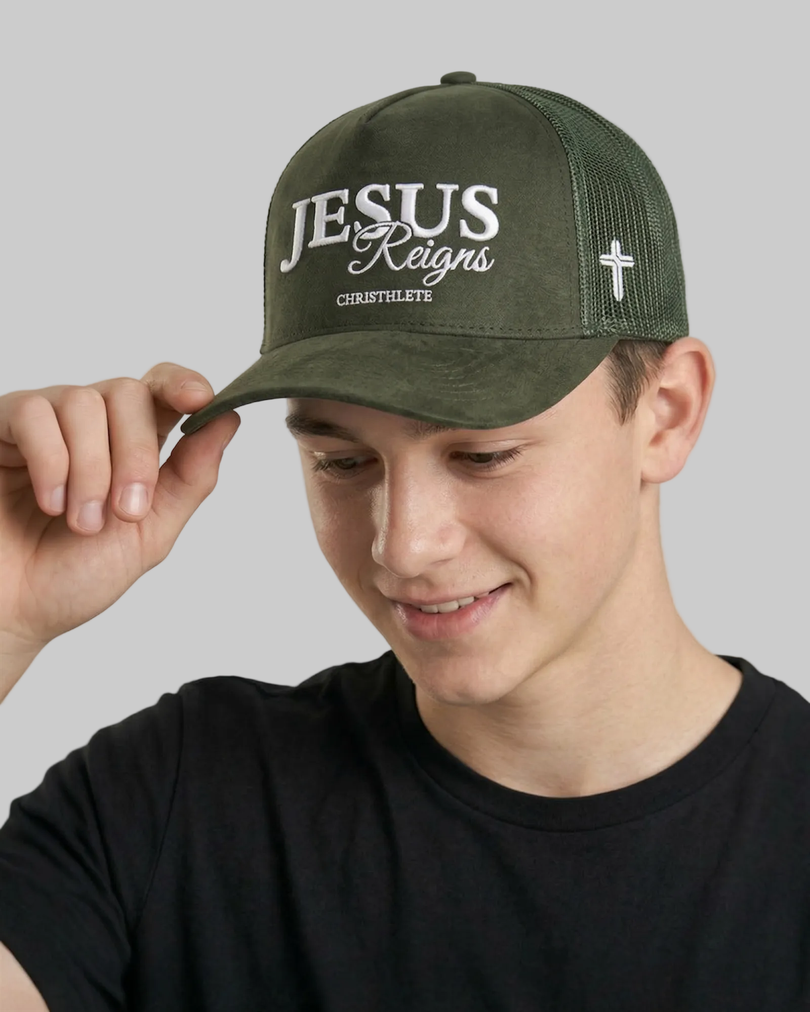 Person wearing a green cap with 'Jesus Reigns' text on a plain background