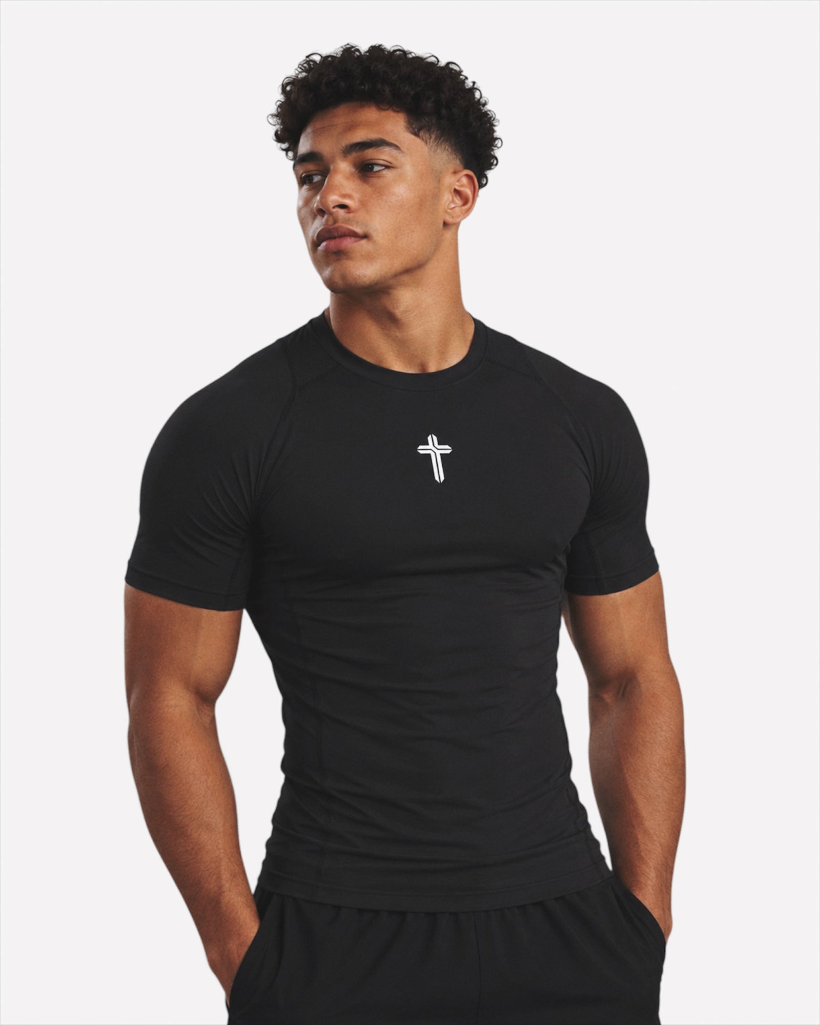 Image of A man wearing a black short-sleeve compression shirt with a small white cross logo on the chest, photographed against a light gray studio background.