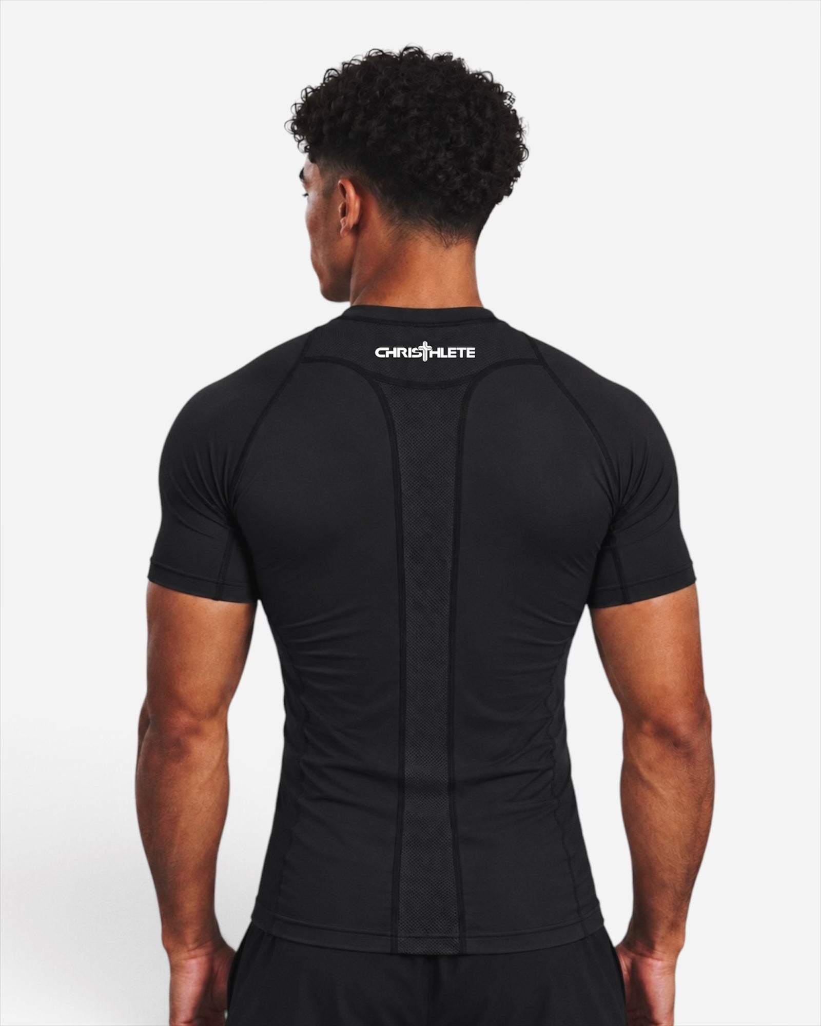 Image of A man viewed from the back wearing a black short-sleeve athletic compression shirt with a white CHRISTHLETE logo on the upper back, set against a plain light gray studio background.