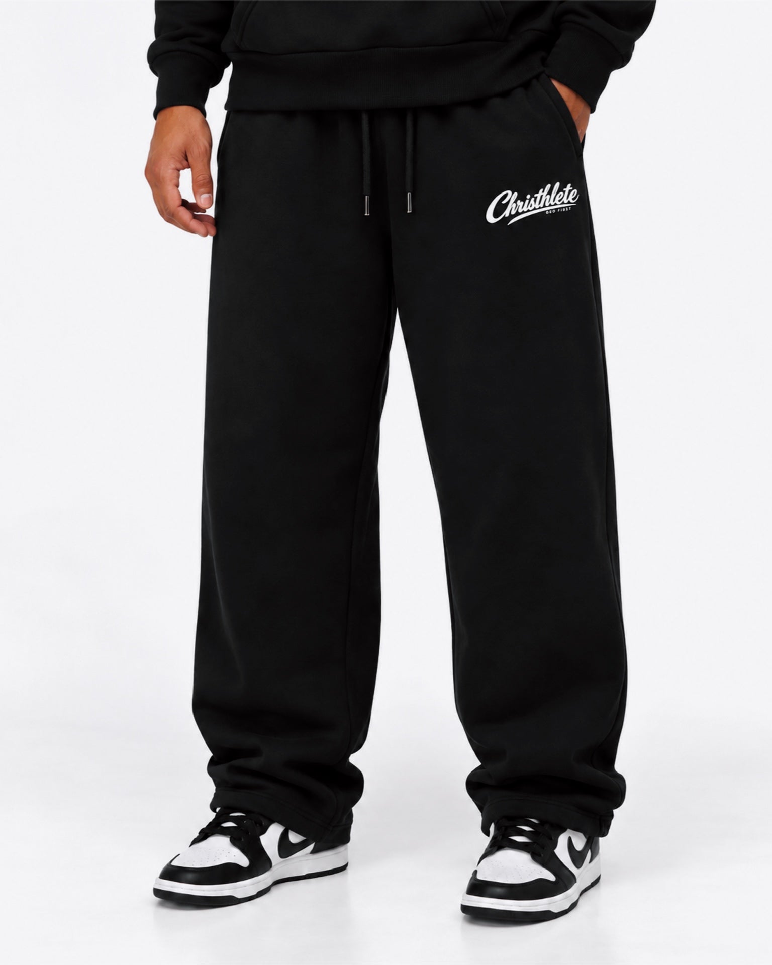 Image of Black sweatpants with a white 'Christhlete God First' logo on the left thigh, shown on a model wearing black sneakers against a white studio background.