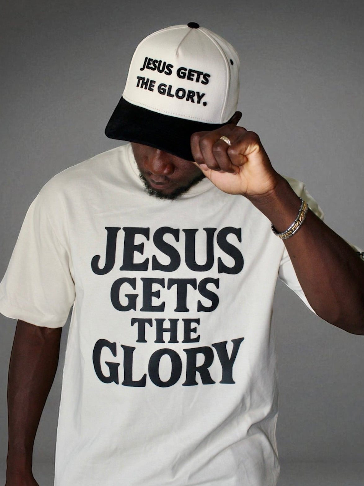Image of Person wearing a beige t-shirt and cap with 'Jesus Gets the Glory' text on a gray background