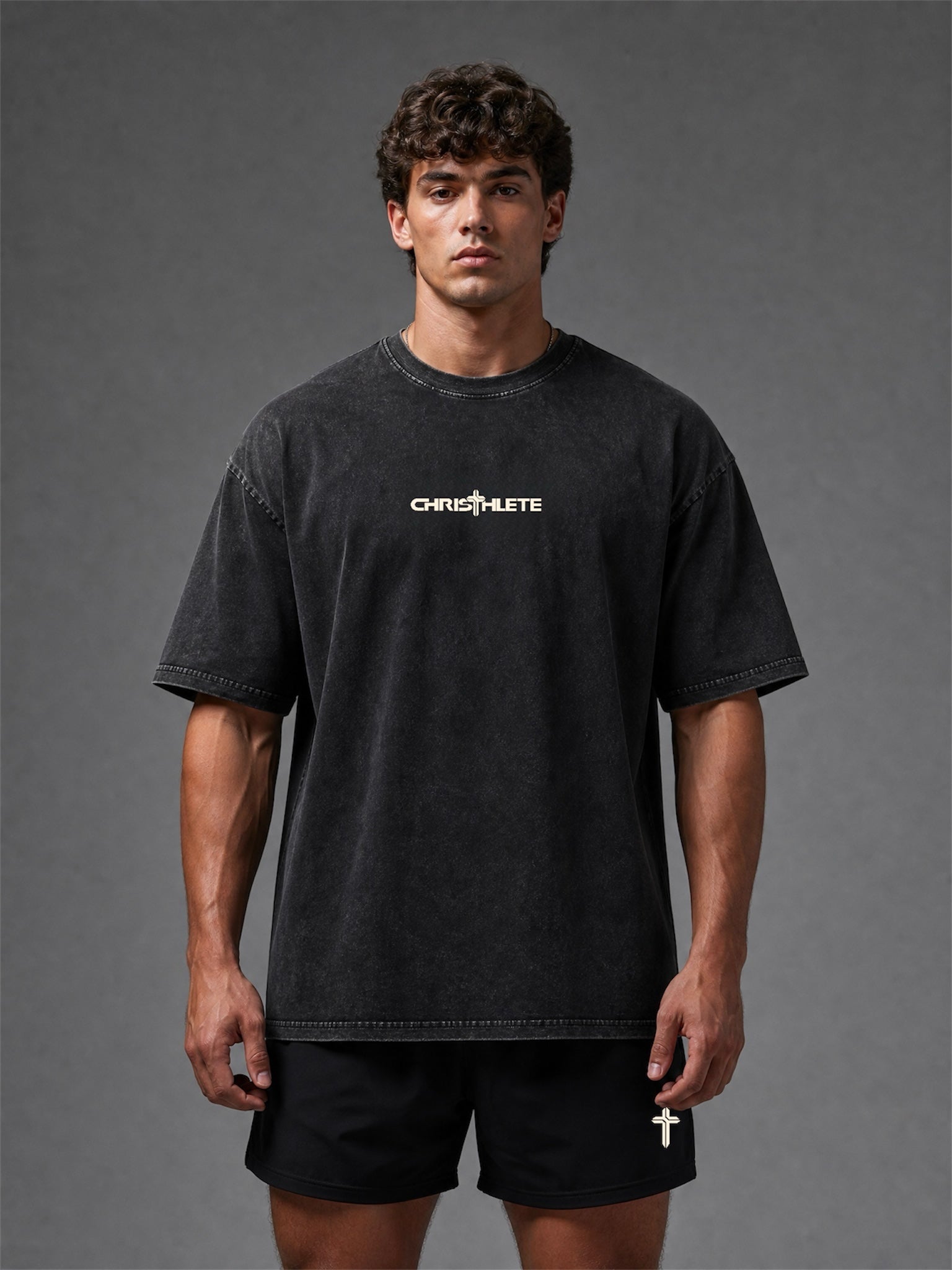 Image of A male model wearing a washed black short-sleeve t-shirt with a white 'CHRISTHLETE' logo across the chest, paired with black shorts, against a dark gray studio background.