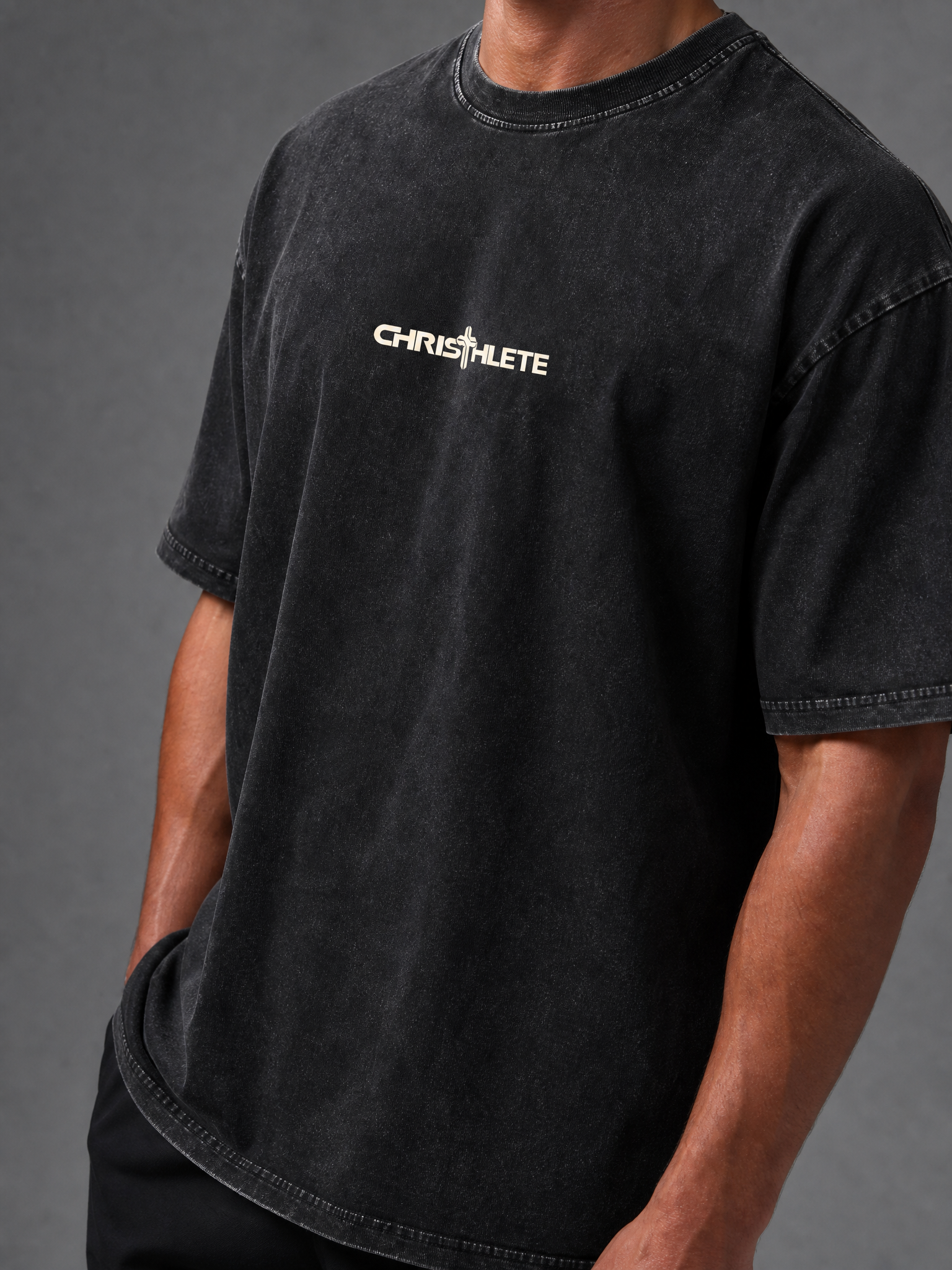 Image of A close-up of a person wearing a faded black crewneck t-shirt with a white 'CHRISTHLETE' logo printed across the chest, set against a dark gray studio background.