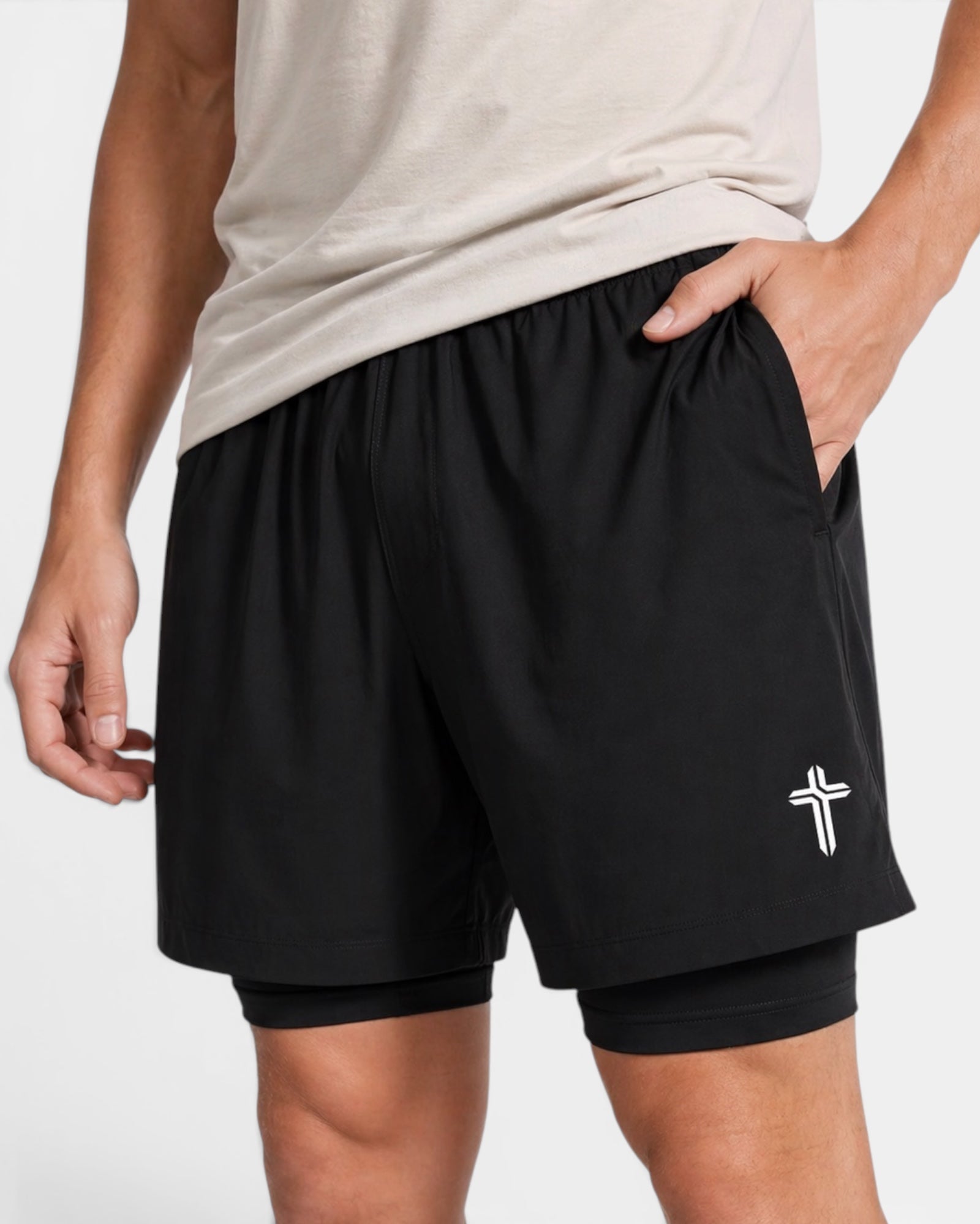 Image of Black athletic shorts with a white logo worn by a person on a light gray background