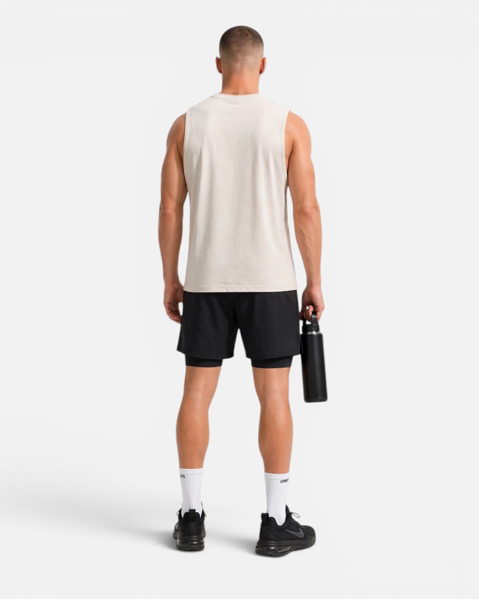 Image of Man wearing a beige sleeveless shirt and black shorts holding a water bottle on a white background