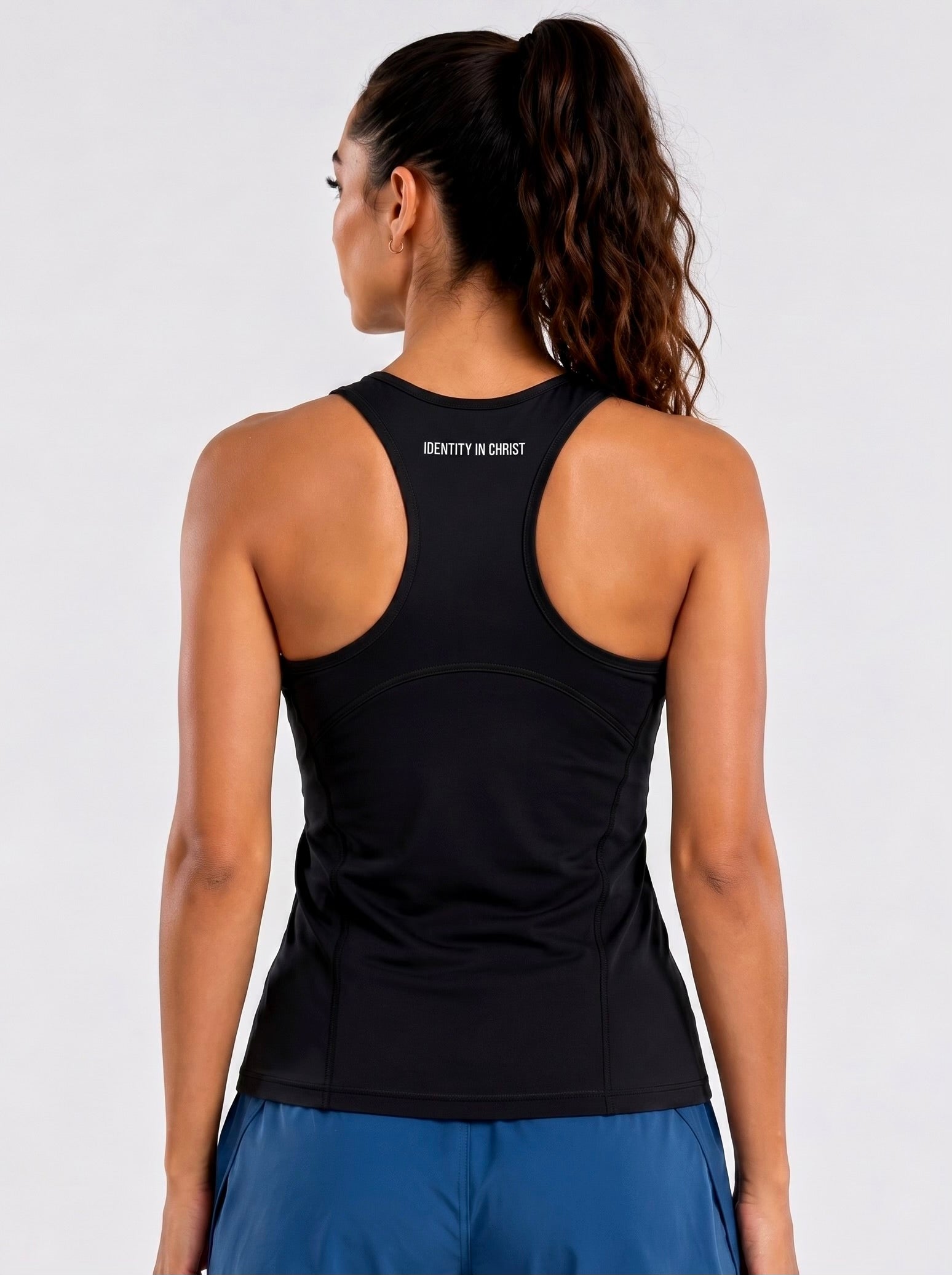 Image of Person wearing a black tank top with 'IDENTITY IN CHRIST' text on the back against a white background