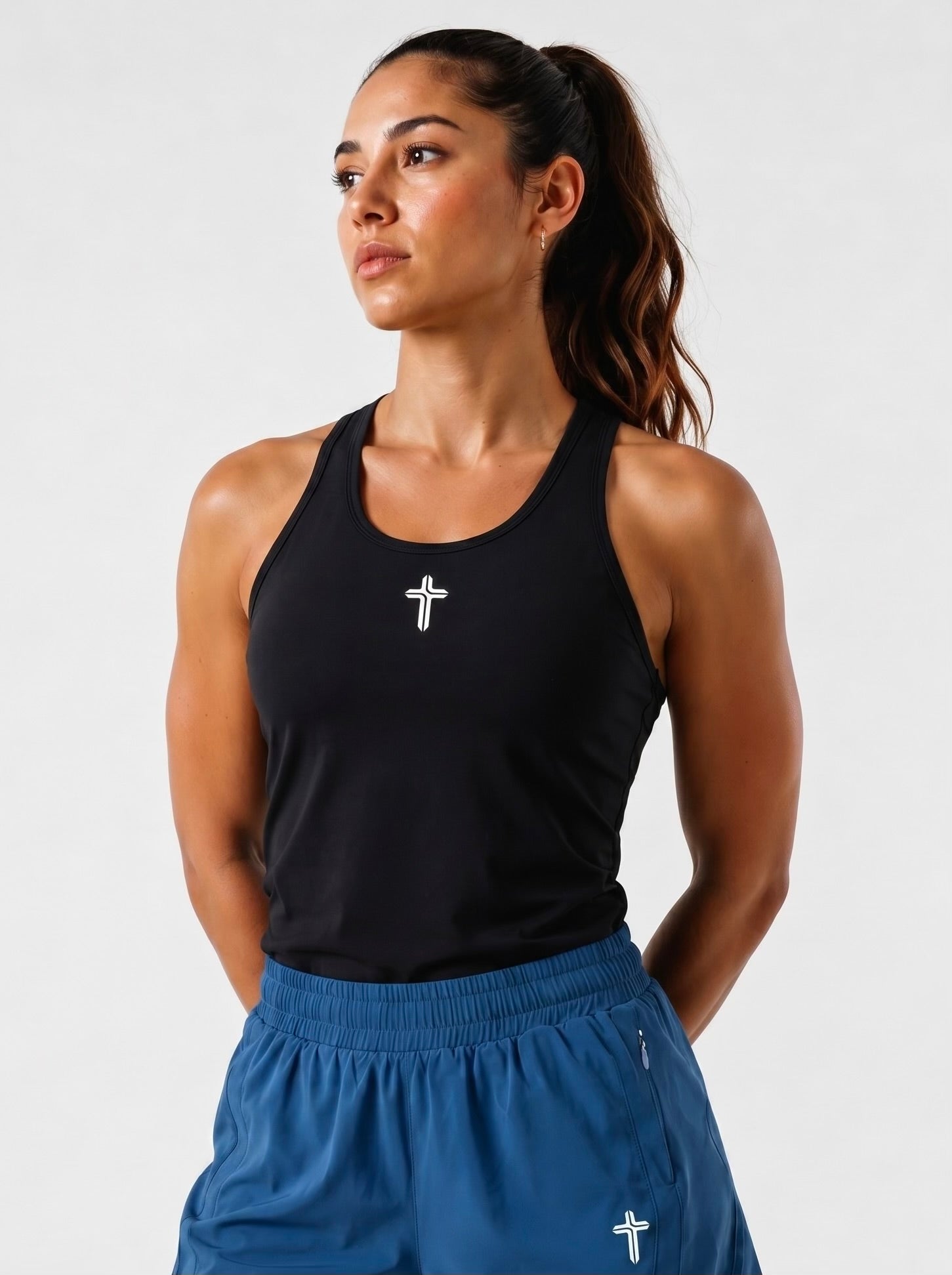 Image of Woman wearing a black tank top with cross logo and blue shorts with a white background